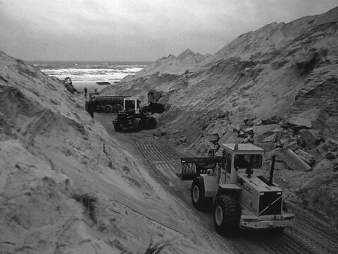 Zwartwit-foto met graafmachines in de duinen, de zee op de achtergrond